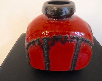 Könnte beinhalten: Eine rote Keramikvase mit einer strukturierten schwarzen Glasur. Die Vase hat eine abgerundete quadratische Form und eine breite Öffnung.