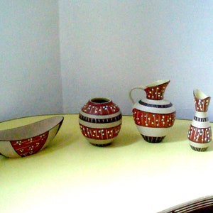 Könnte beinhalten: Ein Set aus vier Keramikvasen mit einem geometrischen Muster in Braun, Weiß und Rot. Die Vasen sind auf einer gelben Oberfläche angeordnet.