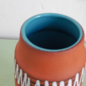 May include: A terracotta ceramic vase with a blue glaze inside. The vase has a white and black geometric pattern around the outside.