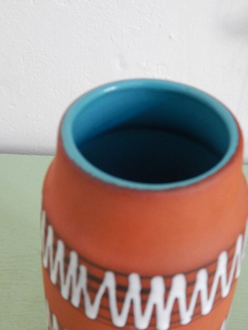 May include: A terracotta ceramic vase with a blue glaze inside. The vase has a white and black geometric pattern around the outside.