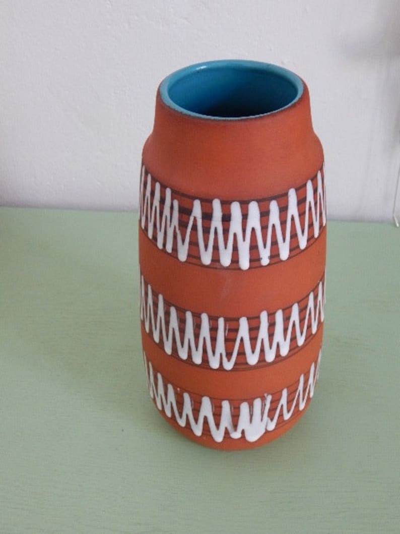 May include: A terracotta ceramic vase with a turquoise blue rim and white wavy lines around the body.