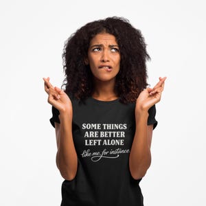 Könnte beinhalten: Schwarzes T-Shirt mit dem weißen Text "SOME THINGS ARE BETTER LEFT ALONE like me for instance". Eine Person mit gekreuzten Fingern und einem nachdenklichen Gesichtsausdruck trägt das Shirt.