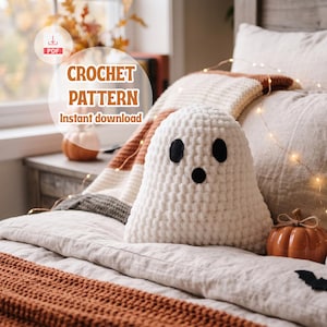 Può includere: Un fantasma all'uncinetto bianco con occhi e bocca in feltro nero, con il testo CROCHET PATTERN Instant download. Il fantasma è posizionato su un letto con una coperta a righe e piccole zucche arancioni, illuminato da luci a stringa.