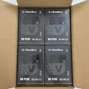 May include: Four black V6 PLUS media player boxes are stacked inside a cardboard box. Each box features the "vSeeBox" logo, a large "V" graphic, and icons indicating 4K, HDR, and other features. The boxes are arranged neatly, ready for shipment.