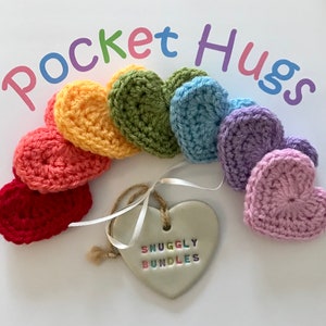 May include: A rainbow of crocheted hearts with the text "Pocket Hugs" and a white heart with the text "Snuggly Bundles".