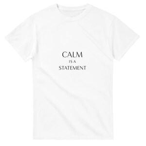 Könnte beinhalten: Weißes T-Shirt mit dem schwarzen Text "CALM IS A STATEMENT" mittig auf der Vorderseite. Das T-Shirt hat kurze Ärmel und einen Rundhalsausschnitt.