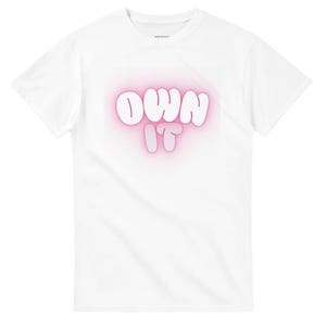 Könnte beinhalten: Weißes T-Shirt mit dem Schriftzug "OWN IT" in einer Bubble-Schrift. Der Text ist weiß umrandet und hat einen rosa Schein. Das Shirt besteht aus einem weichen Material.