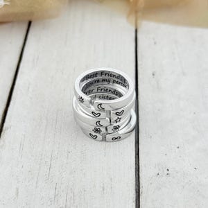 K&ouml;nnte beinhalten: Stapel von f&uuml;nf silbernen Ringen mit gravierten Botschaften und Symbolen. Der oberste Ring tr&auml;gt die Aufschrift "Best Friends Forever You're my person". Die anderen Ringe haben Symbole wie einen Stern, einen Mond, ein Herz, eine Blume und ein Unendlichkeitszeichen.