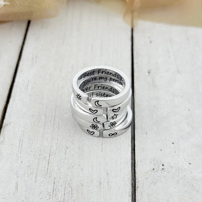 K&ouml;nnte beinhalten: Stapel von f&uuml;nf silbernen Ringen mit gravierten Botschaften und Symbolen. Der oberste Ring tr&auml;gt die Aufschrift "Best Friends Forever You're my person". Die anderen Ringe haben Symbole wie einen Stern, einen Mond, ein Herz, eine Blume und ein Unendlichkeitszeichen.