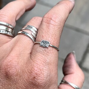 Może przedstawiać: Srebrny pierścionek z małym wisiorkiem w kształcie aparatu fotograficznego. Wisiorkiem aparatu fotograficznego ma serce w wizjerze.
