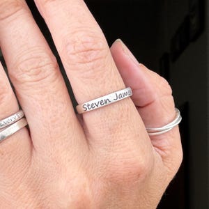 May include: A silver ring with the inscription "Steven James" on a person's finger.