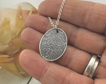 Puede incluir: Collar de plata con un colgante ovalado con un diseño de huella digital detallado.