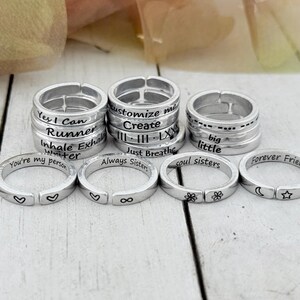 K&ouml;nnte beinhalten: Ein Set aus zehn silbernen Ringen mit verschiedenen gravierten Botschaften, darunter "Yes I Can", "Runner", "Customize Me", "Create", "Just Breathe", "Always Sisters", "Soul Sisters", "Big Little", "You're My Person" und "Forever Friends".