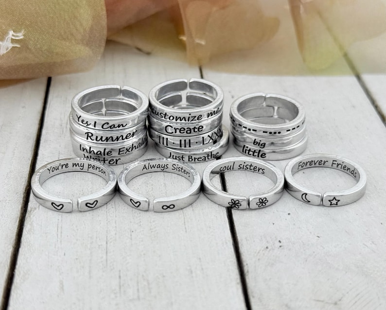 K&ouml;nnte beinhalten: Ein Set aus zehn silbernen Ringen mit verschiedenen gravierten Botschaften, darunter "Yes I Can", "Runner", "Customize Me", "Create", "Just Breathe", "Always Sisters", "Soul Sisters", "Big Little", "You're My Person" und "Forever Friends".
