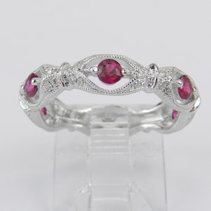 Könnte beinhalten: Ein silberner Bandring mit einem filigranen Design mit vier roten Edelsteinen und kleineren weißen Edelsteinen.