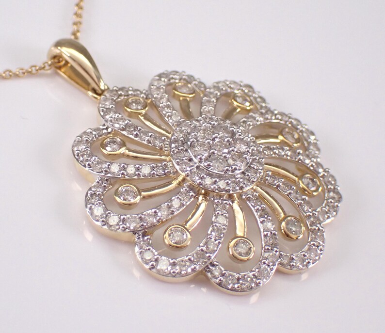 May include: A gold-toned pendant necklace featuring a flower design. The pendant has a central cluster of small, clear stones surrounded by petal-shaped sections, each outlined with more stones. The necklace chain is also gold-toned.