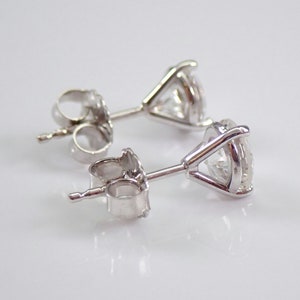 May include: A pair of stud earrings with clear, round-cut gemstones set in a silver metal. The earrings are displayed on a white surface, showcasing their sparkle and design. The earrings have a classic, elegant style.