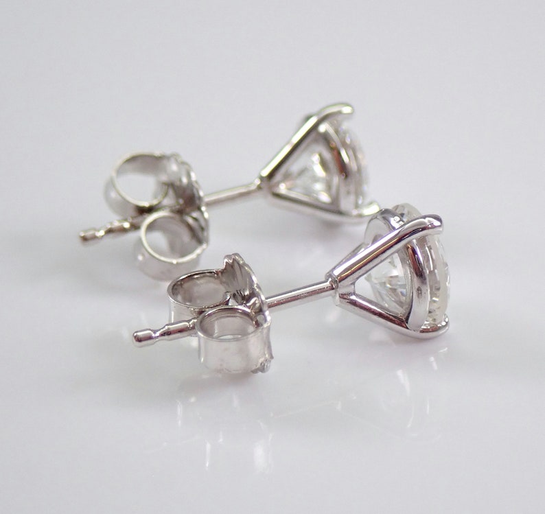 May include: A pair of stud earrings with clear, round-cut gemstones set in a silver metal. The earrings are displayed on a white surface, showcasing their sparkle and design. The earrings have a classic, elegant style.