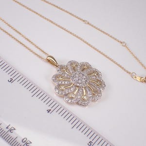 May include: A gold-toned necklace with a floral pendant. The pendant features a central cluster of small, clear stones surrounded by a detailed, openwork design. The necklace is on a white surface.