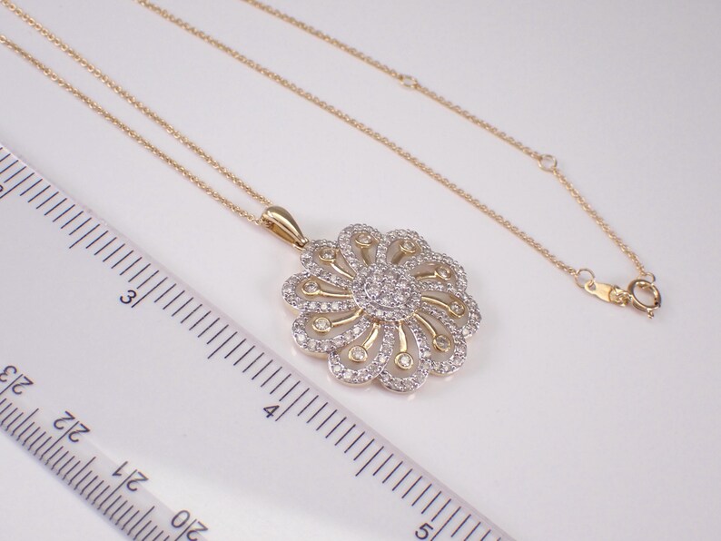 May include: A gold-toned necklace with a floral pendant. The pendant features a central cluster of small, clear stones surrounded by a detailed, openwork design. The necklace is on a white surface.