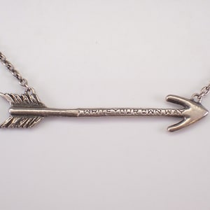 May include: Silver arrow pendant necklace with the text "WRITE YOUR OWN WAY". The arrow has a feathered end and a pointed tip. The chain is a delicate silver link.