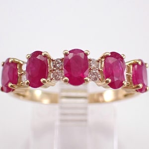 May include: A gold ring with five oval rubies and small diamonds. The rubies are a deep red, and the ring has a polished finish. The ring is set on a gold band.