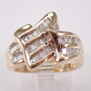 May include: A gold-toned ring with a unique, asymmetrical design. The ring features multiple rows of baguette-cut diamonds, adding sparkle and dimension. The band curves and wraps around the finger, creating a modern look.