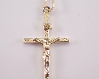 Op de afbeelding: Een gouden crucifix hanger met een gedetailleerde figuur van Jezus op een kruis met getextureerde accenten op de armen en de verticale balk. Een klein vaandel bovenaan het kruis bevat de inscriptie INRI en er is een oogje bevestigd.