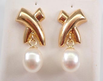 May include: Gold earrings with a pearl drop. The earrings feature a gold design that resembles a stylized 'X'.