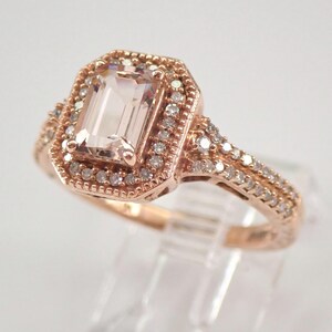 May include: A rose gold engagement ring with a large, rectangular, light pink morganite gemstone surrounded by a halo of smaller diamonds. The band is also set with diamonds.