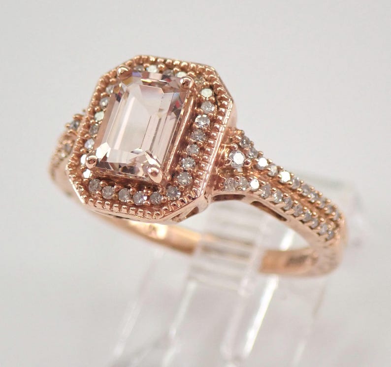 May include: A rose gold engagement ring with a large, rectangular, light pink morganite gemstone surrounded by a halo of smaller diamonds. The band is also set with diamonds.