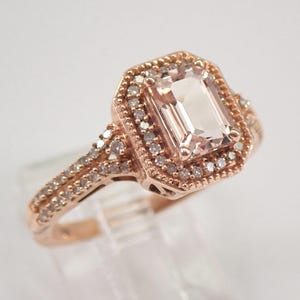 May include: A rose gold engagement ring with a large, rectangular, light pink morganite gemstone surrounded by a halo of smaller diamonds. The band is also set with smaller diamonds.
