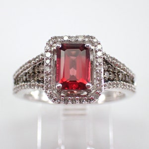 May include: A silver ring featuring a red gemstone set within a halo of smaller diamonds. The band is embellished with smaller diamonds.