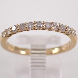 Könnte beinhalten: Ein goldener Ring mit einer Reihe kleiner, klarer Edelsteine. Der Ring hat eine polierte, reflektierende Oberfläche. Die Edelsteine sind gleichmäßig über die Oberseite des Rings verteilt.