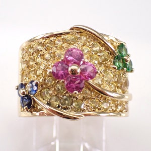 May include: A gold ring with a flower design set with pink, blue, and green gemstones. The ring is covered in small yellow gemstones.