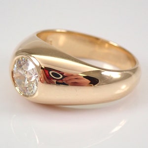 May include: A gold ring with a large, round, clear gemstone set in a smooth, rounded bezel. The ring has a wide band.