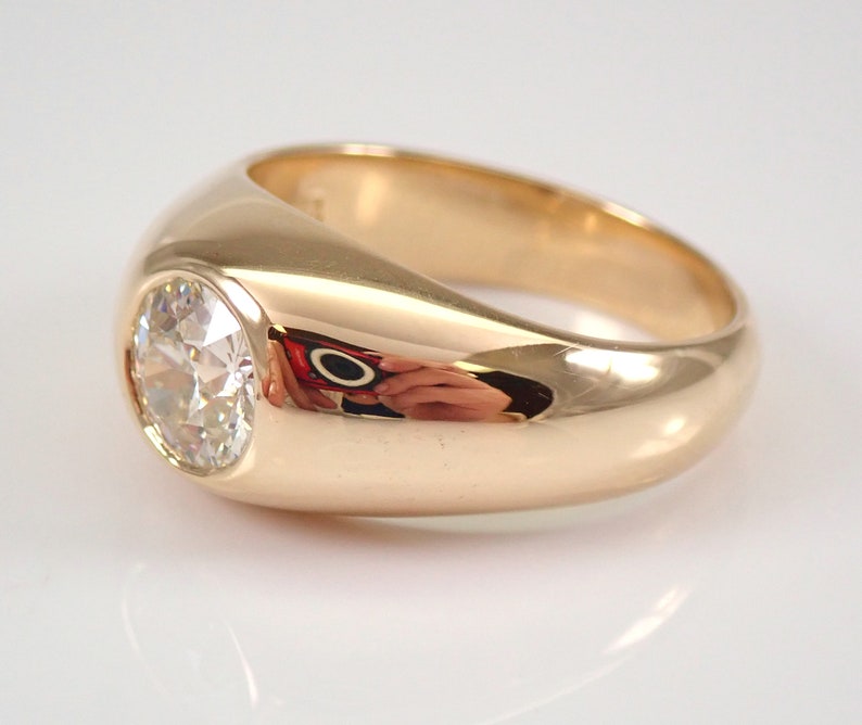 May include: A gold ring with a large, round, clear gemstone set in a smooth, rounded bezel. The ring has a wide band.