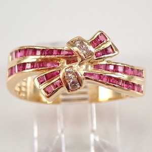 以下が含まれることがあります： ルビーのボウデザインのゴールドリング。ボウは小さな正方形にカットされたルビーで作られており、小さな丸いダイヤモンドでアクセントが付けられています。