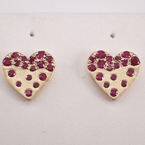 Peut inclure: Une paire de boucles d'oreilles en forme de cœur. Les boucles d'oreilles sont dorées avec une finition texturée. La moitié supérieure de chaque cœur est recouverte de petites pierres précieuses rouges rondes, tandis que de plus grandes pierres rouges sont dispersées.