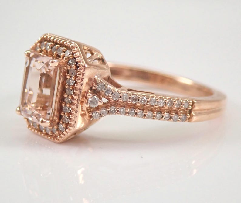 May include: A rose gold engagement ring with a large, square-cut, light pink gemstone surrounded by a halo of smaller diamonds. The band is also set with smaller diamonds.