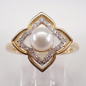 May include: A gold ring with a pearl set in a diamond-encrusted flower design.
