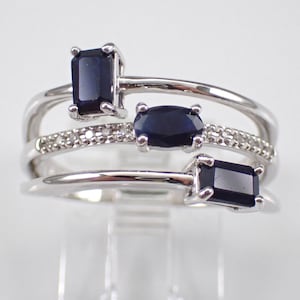 Könnte beinhalten: Ein silberner Ring mit drei blauen Edelsteinen und einer Reihe kleiner, klarer Edelsteine. Der Ring hat ein dreifaches Banddesign.