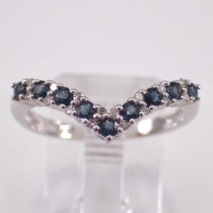Könnte beinhalten: Ein silberfarbener Ring mit V-förmigem Design. Der Ring ist mit einer Reihe dunkelblauer Edelsteine und kleinen weißen Edelsteinen besetzt. Der Ring ist vor einem weißen Hintergrund platziert.