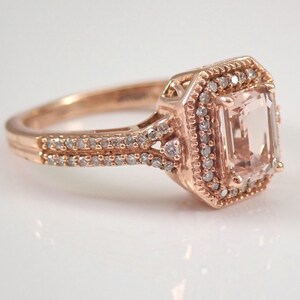May include: A rose gold engagement ring with a large, light pink, emerald-cut gemstone surrounded by a halo of smaller diamonds. The band is also set with smaller diamonds.