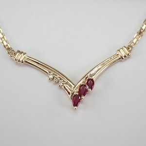 May include: A gold necklace with a V-shaped pendant set with three red gemstones and small diamonds.