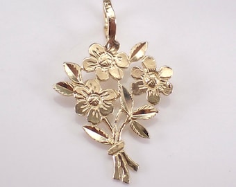 May include: A gold pendant shaped like a small bouquet of three flowers with textured petals and leaves. The flowers are arranged in a cluster with stems tied together at the bottom. A small, hinged bail is attached to the top for hanging.