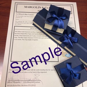 May include: A close-up of a blue velvet jewelry box with a white satin interior. The box is tied with a blue ribbon and bow. The box contains a 14K yellow gold ring with a blue topaz and diamonds. The ring is described as having two pear-shaped blue topaz and twenty-three round diamonds. The diamonds are H color, SI clarity and weigh 1 carat. The blue topaz measure 7.5 x 5.5 mm each and weigh 2 1/2 carats. The ring weighs 4.3 grams. The appraisal is signed by David Margolin, GIA Diamond Graduate, 800 Bustleton Pike, Richboro PA 18954.