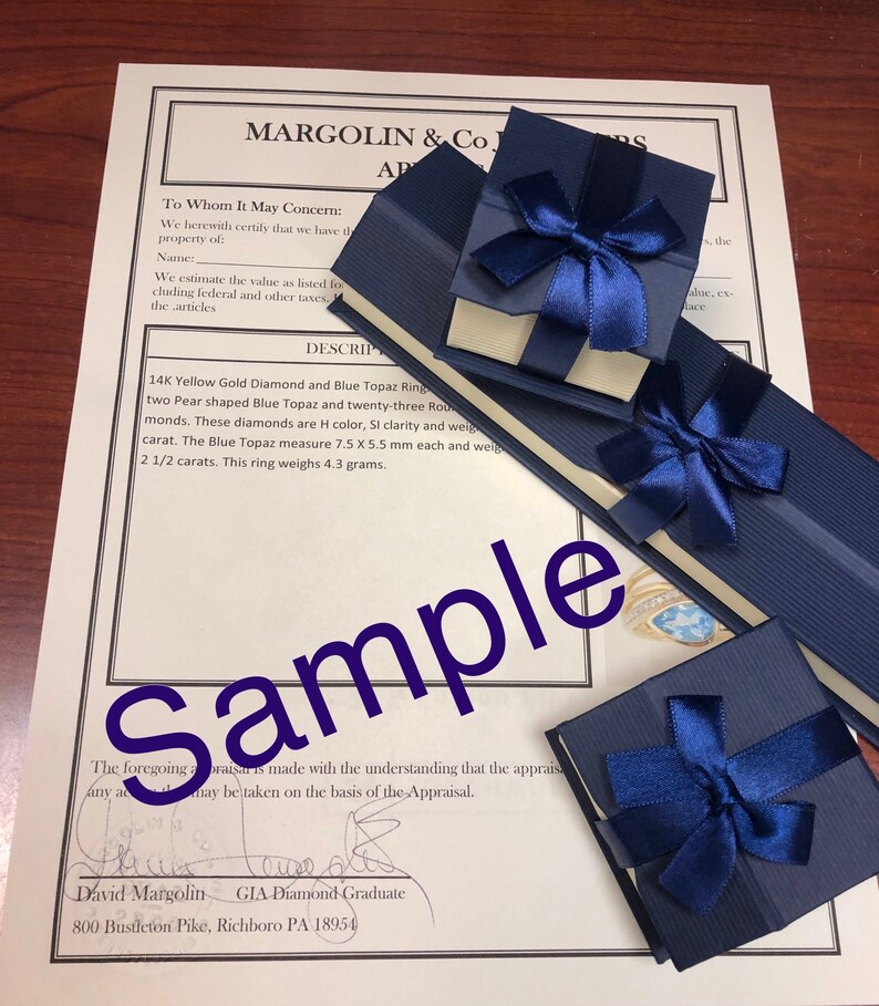 May include: A close-up of a blue velvet jewelry box with a white satin interior. The box is tied with a blue ribbon and bow. The box contains a 14K yellow gold ring with a blue topaz and diamonds. The ring is described as having two pear-shaped blue topaz and twenty-three round diamonds. The diamonds are H color, SI clarity and weigh 1 carat. The blue topaz measure 7.5 x 5.5 mm each and weigh 2 1/2 carats. The ring weighs 4.3 grams. The appraisal is signed by David Margolin, GIA Diamond Graduate, 800 Bustleton Pike, Richboro PA 18954.
