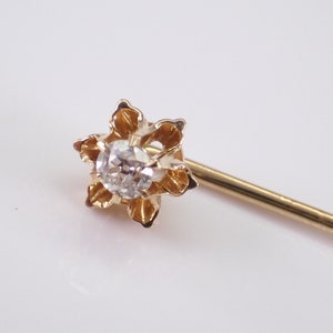 May include: A gold tie tack with a single diamond in the center, surrounded by a flower-shaped design.