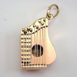 May include: A gold-tone harp charm pendant with a detailed design. The harp has strings and a sound hole. The charm is perfect for a necklace or bracelet.